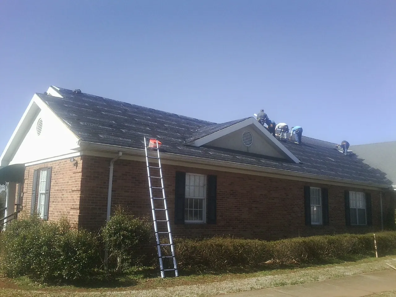 Crew tearing shingles off a brick ranch roof with a ladder set — Metal Roof Repair work by our crew in Reddell