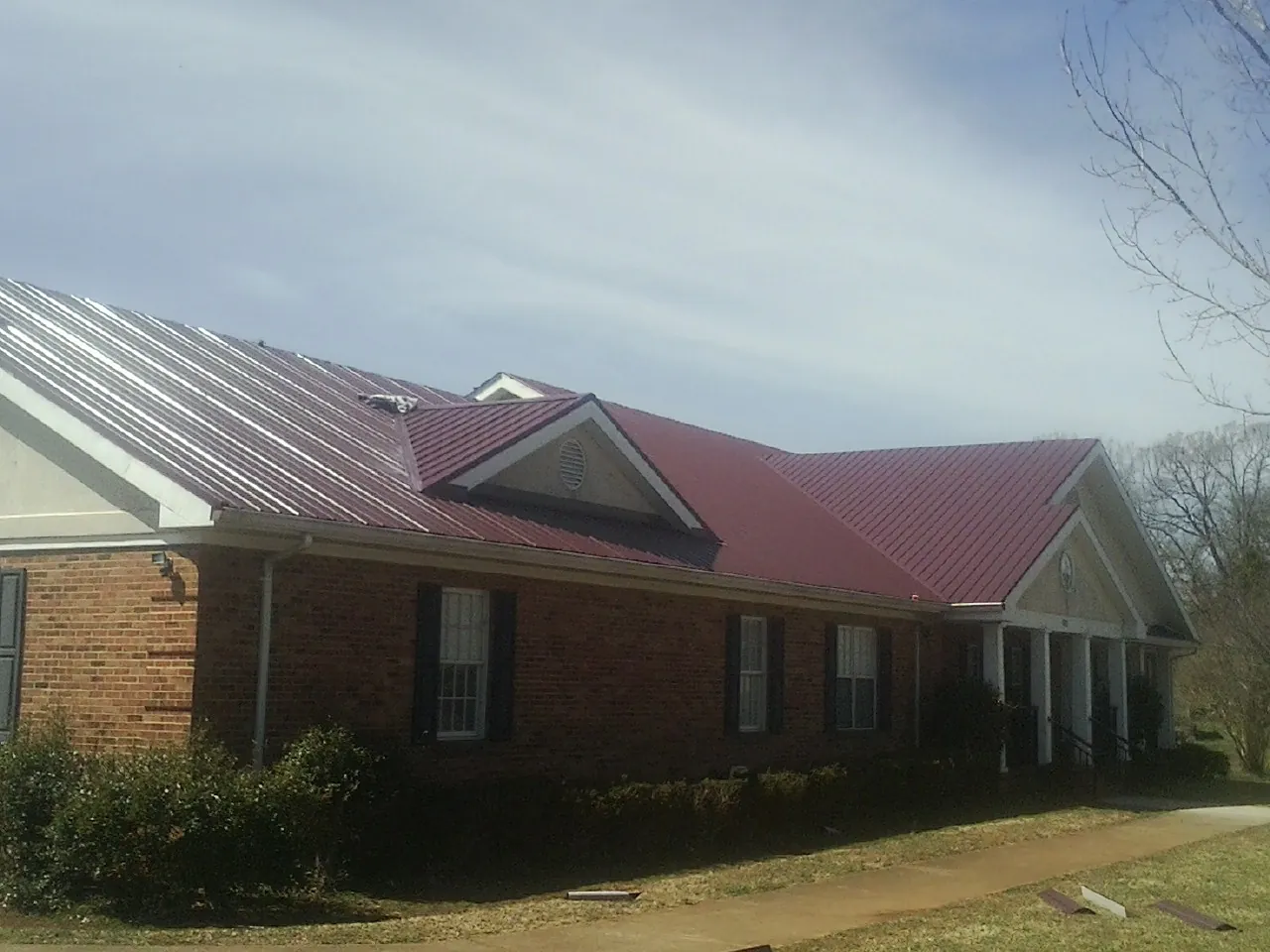 Red metal roof with gabled entries on a long brick building, from a Hail Damage Roof Repair job in Reddell