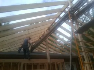 Rafters going up over a new addition with a worker on the wall in Reddell