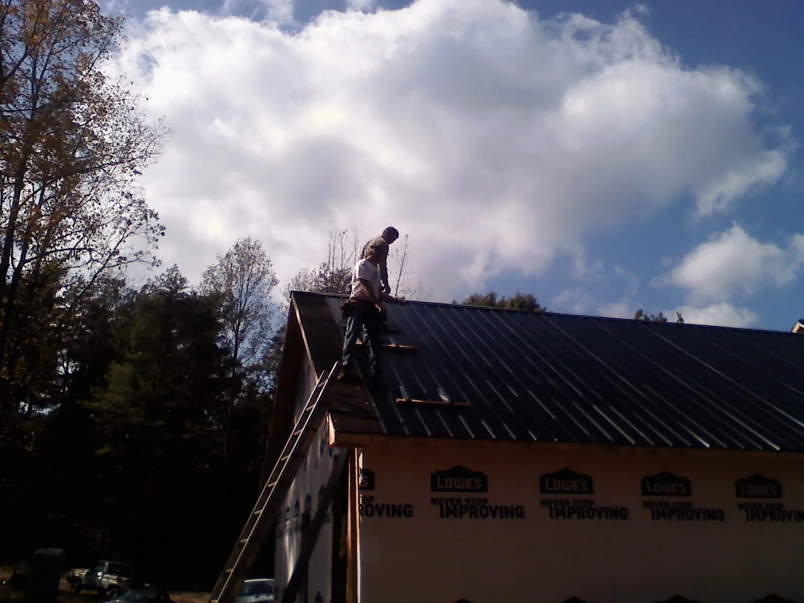Roofer fastening dark metal panels high against a cloudy sky, from a Roof Inspection job in Reddell